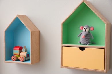 Photo of Stylish house shaped shelves with toys on white wall. Baby room interior design