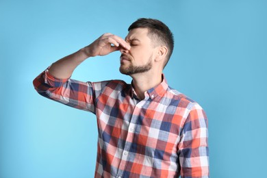 Photo of Man suffering from runny nose on light blue background