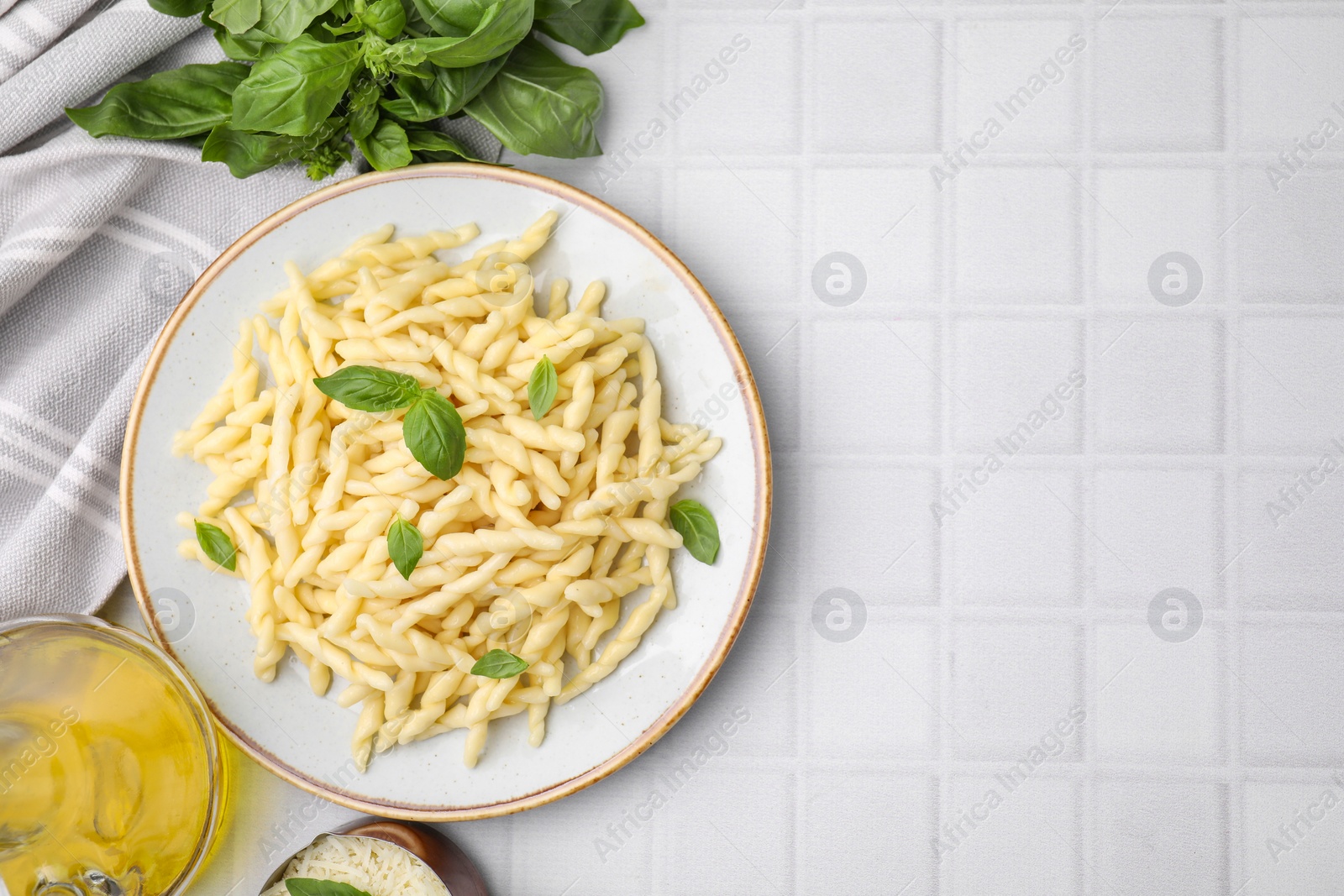 Photo of Plate of delicious trofie pasta with basil leaves on white tiled table, flat lay. Space for text