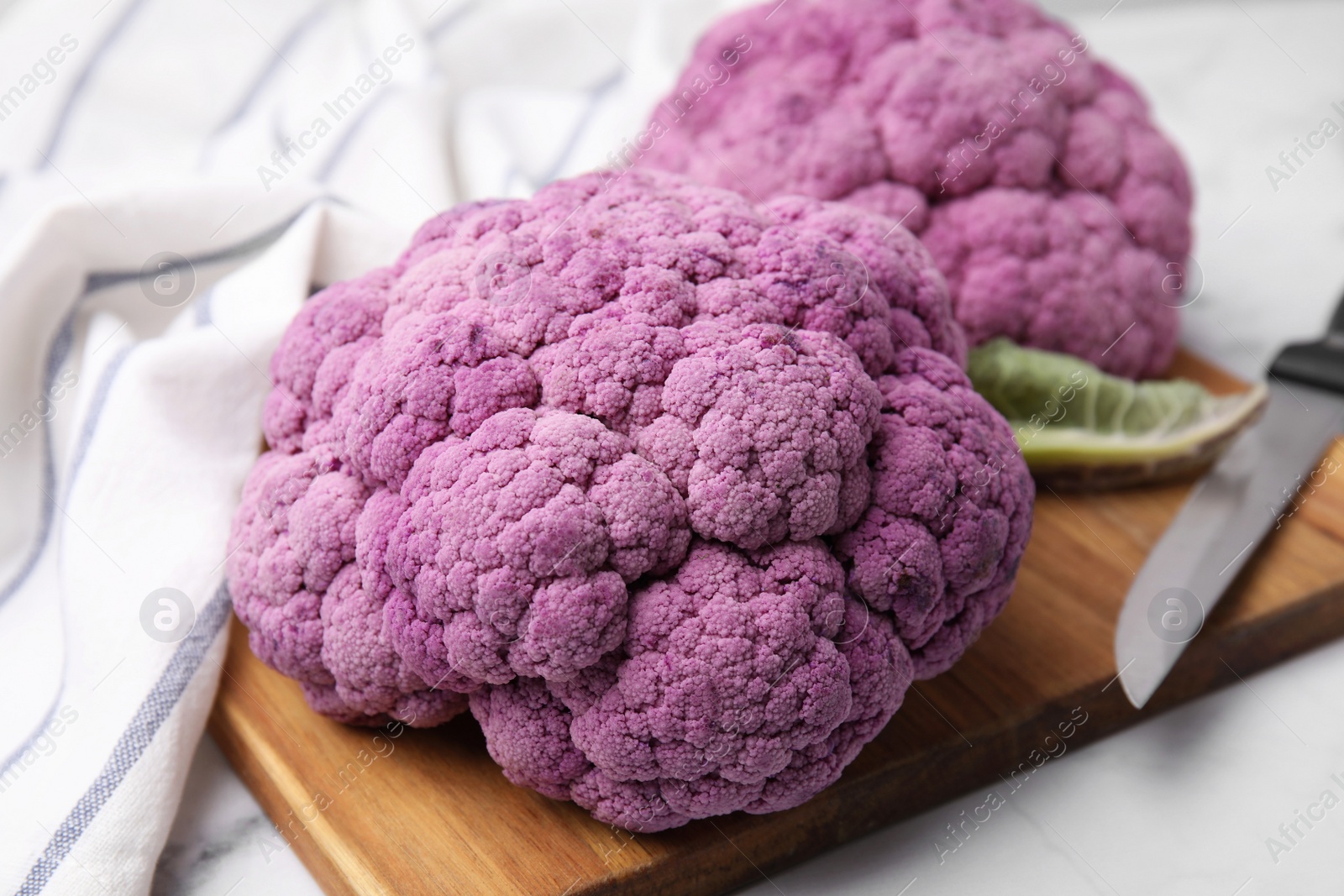 Photo of Fresh cauliflowers, cutting board and knife on white table, closeup