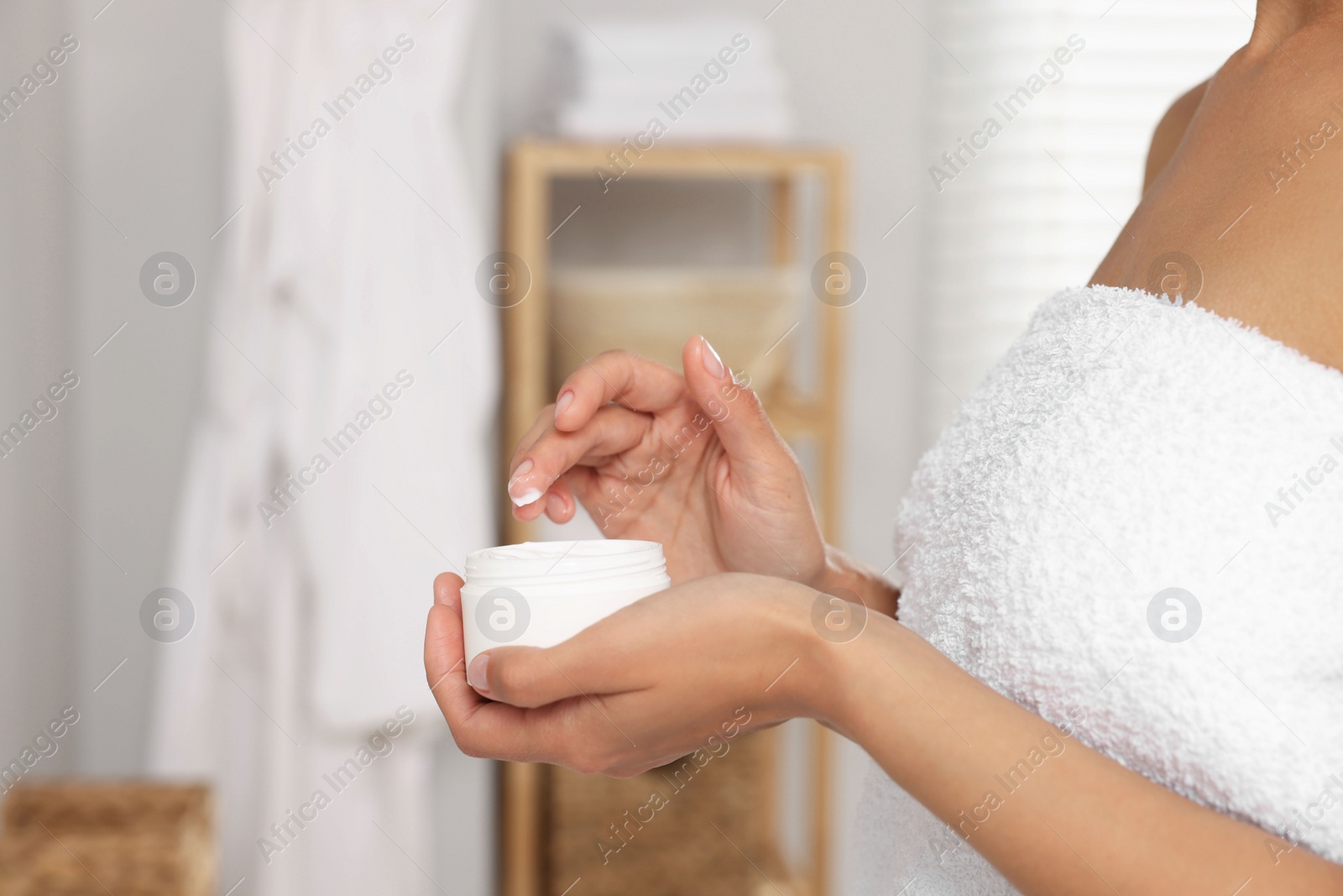 Photo of Woman holding body cream in white jar in bathroom