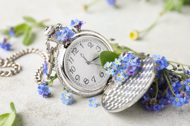 Beautiful blue forget-me-not flowers with pocket watch on light stone table, closeup