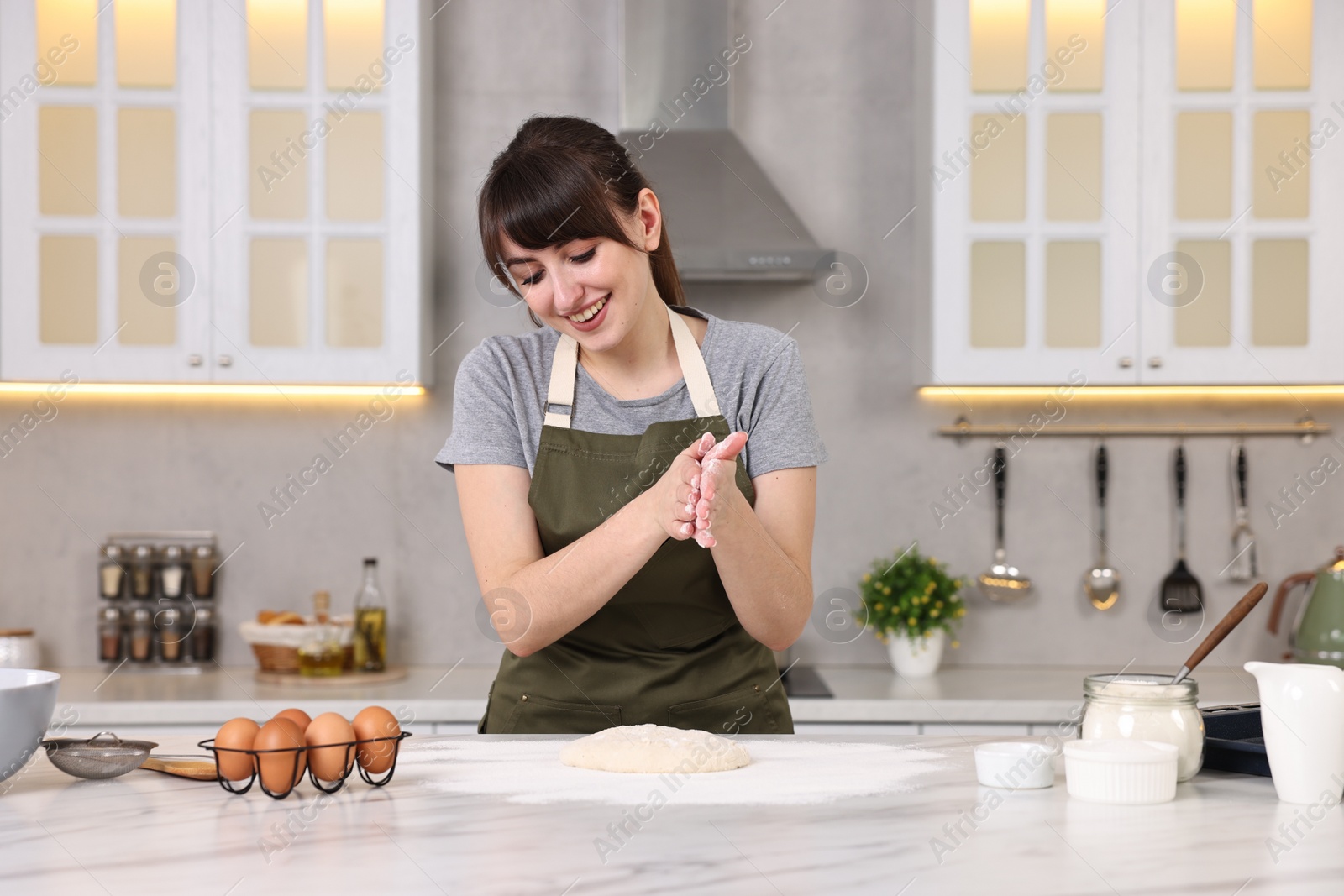 Photo of Happy young housewife making dough at white marble table in kitchen