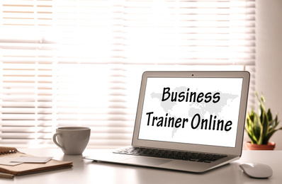 Image of Modern laptop with text BUSINESS TRAINER ONLINE on desk indoors