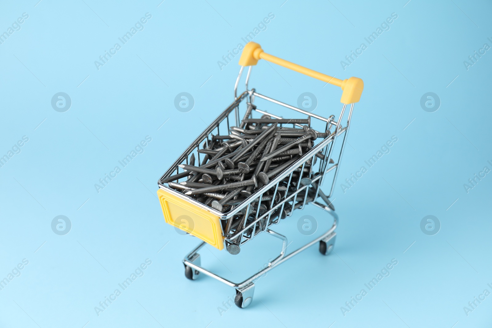 Photo of Metal nails in shopping cart on light blue background