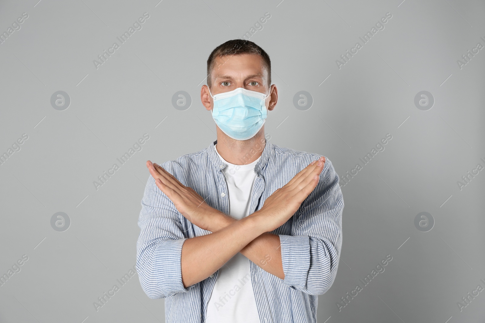 Photo of Man in protective mask showing stop gesture on grey background. Prevent spreading of coronavirus