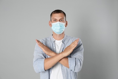 Photo of Man in protective mask showing stop gesture on grey background. Prevent spreading of coronavirus