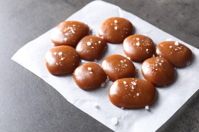 Tasty caramel candies and salt on grey table