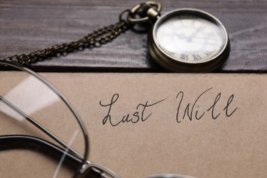 Paper with words Last Will, pocket watch and glasses on wooden table, closeup