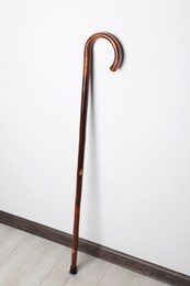 Elegant wooden walking cane near white wall indoors