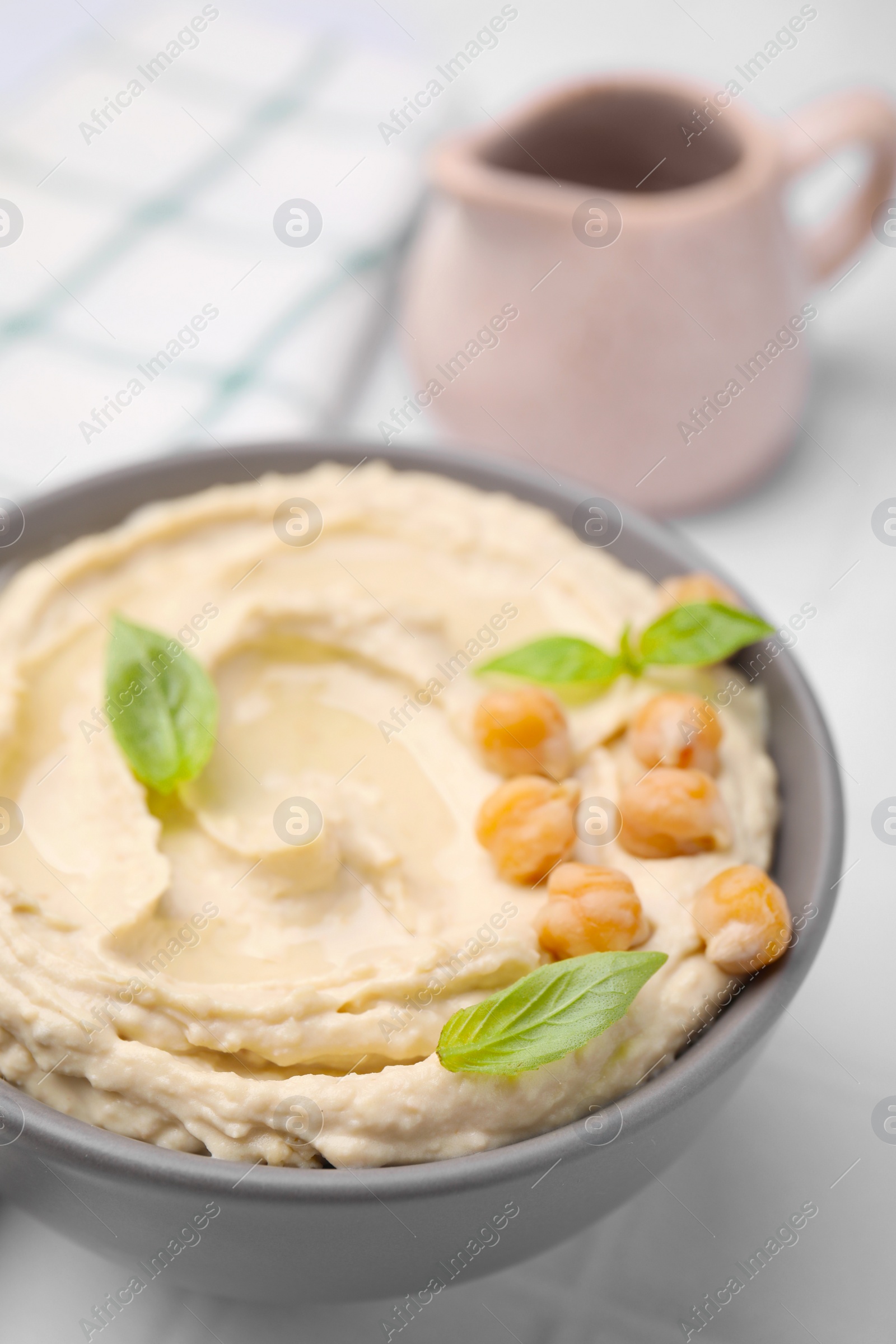 Photo of Delicious hummus with chickpeas served on white tiled table, closeup