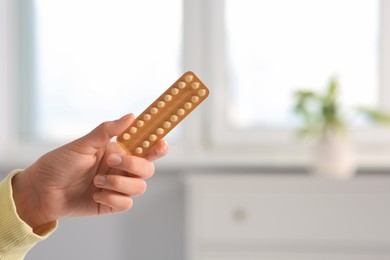 Photo of Woman holding blister of oral contraception pills in bedroom, closeup. Space for text