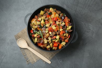 Photo of Delicious ratatouille in baking dish and wooden spoon on grey table, flat lay