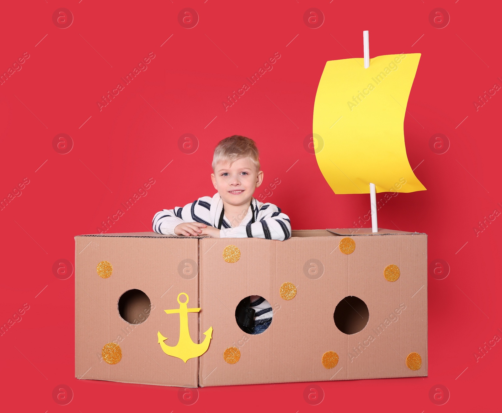 Photo of Little child playing with ship made of cardboard box on red background