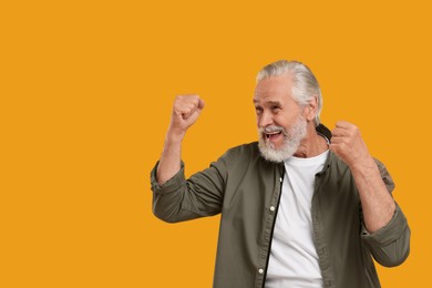 Happy senior sports fan celebrating on yellow background, space for text