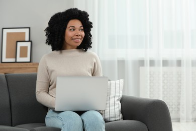 Photo of Happy young woman using laptop on sofa indoors. Space for text