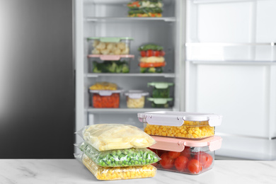 Photo of Different frozen vegetables on white marble table near open refrigerator