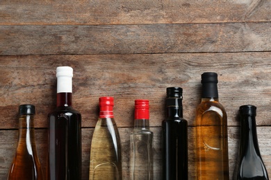 Photo of Bottles with different kinds of vinegar and space for text on wooden background, flat lay