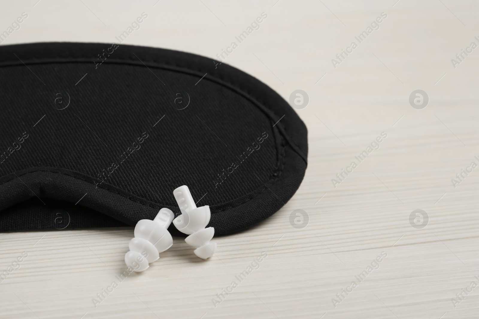 Photo of Pair of ear plugs and sleeping mask on white wooden background