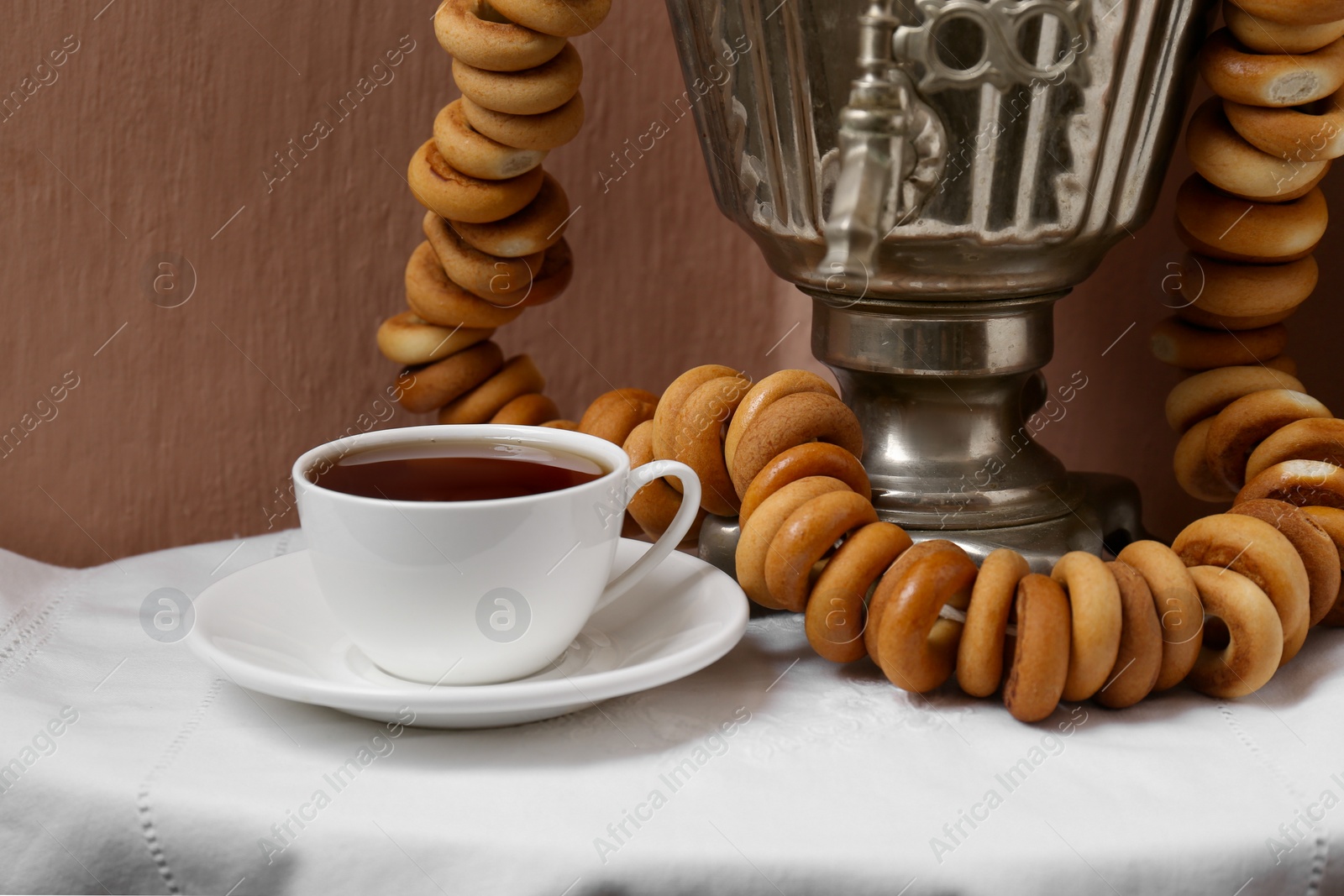 Photo of Vintage samovar, cup of hot drink and dry bagels served on table. Traditional Russian tea ceremony