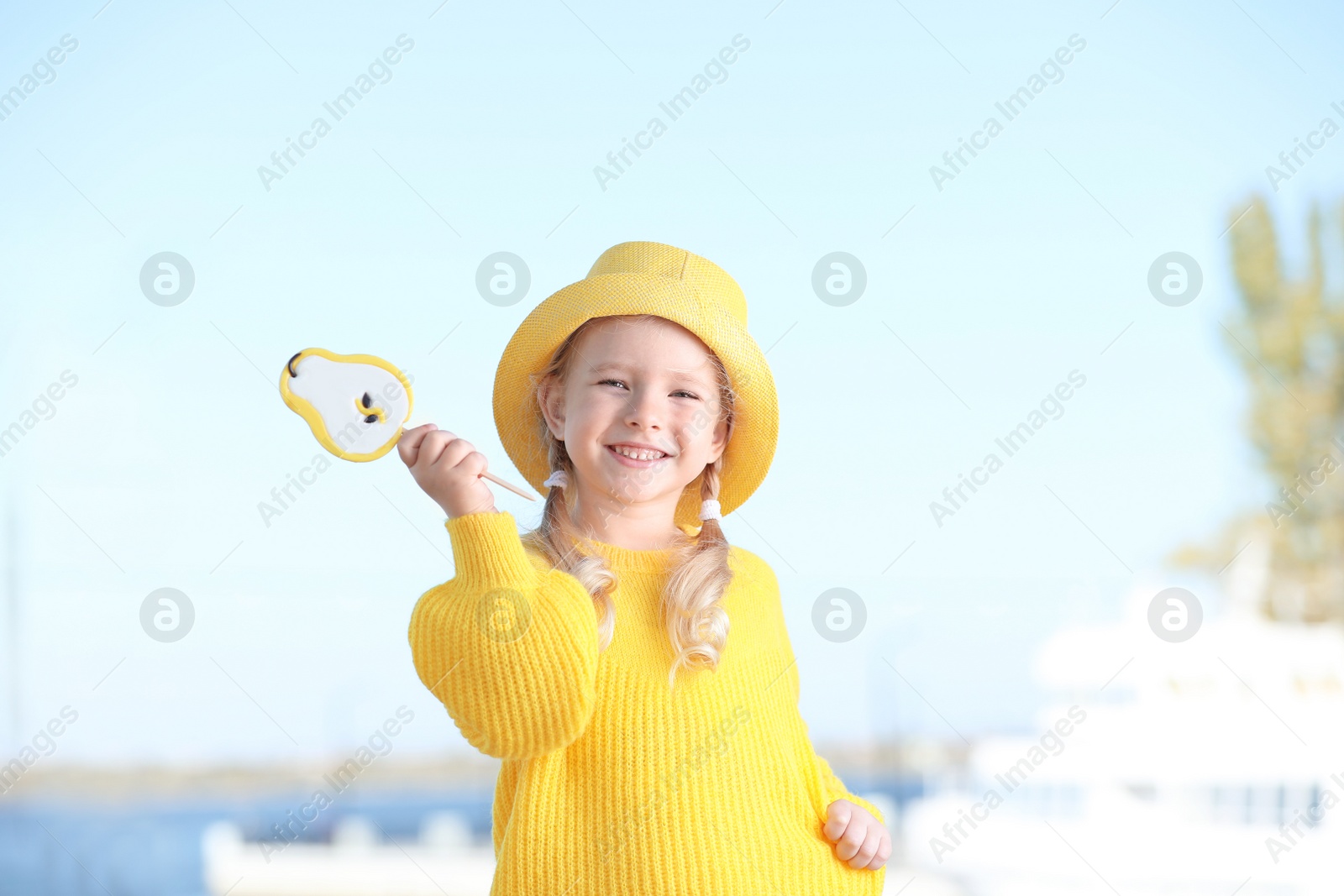 Photo of Cute little girl with tasty candy outdoors