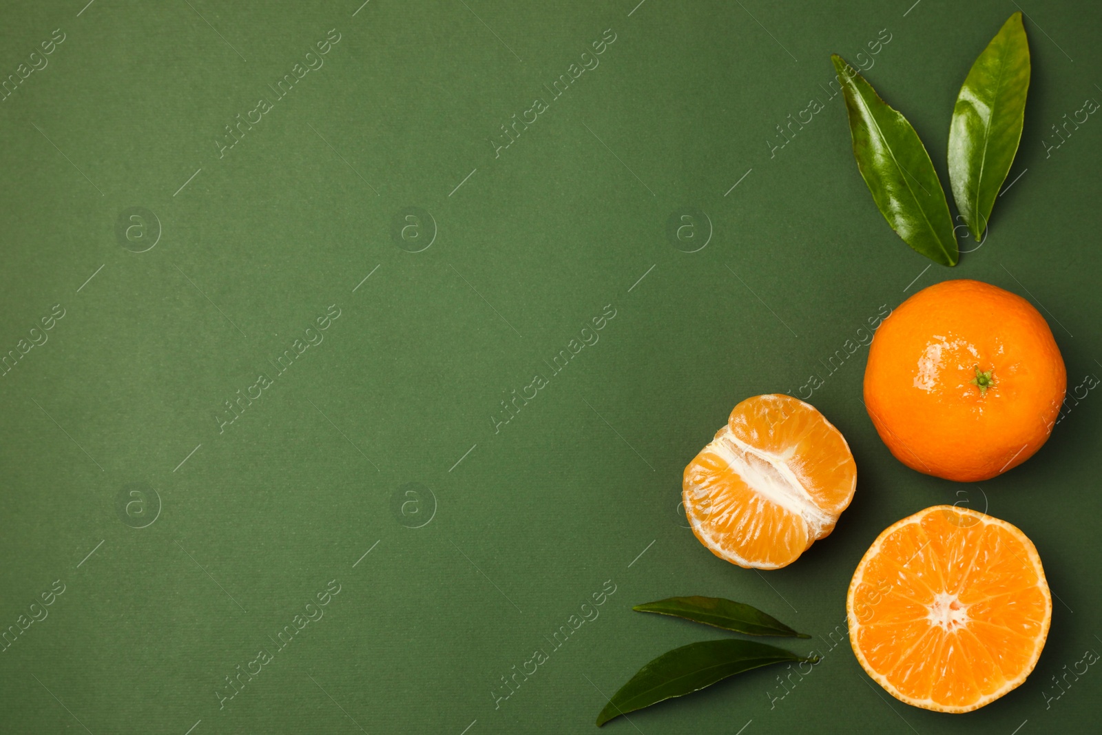 Photo of Delicious tangerines and leaves on green background, flat lay. Space for text