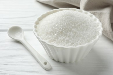 Photo of Granulated sugar in bowl and spoon on white wooden table, closeup