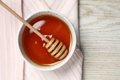 Bowl with tasty honey and dipper on light wooden table, top view. Space for text