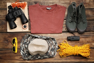 Flat lay composition with wardrobe items and camping equipment on wooden background