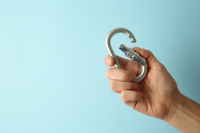 Man with metal carabiner on light blue background, closeup. Space for text