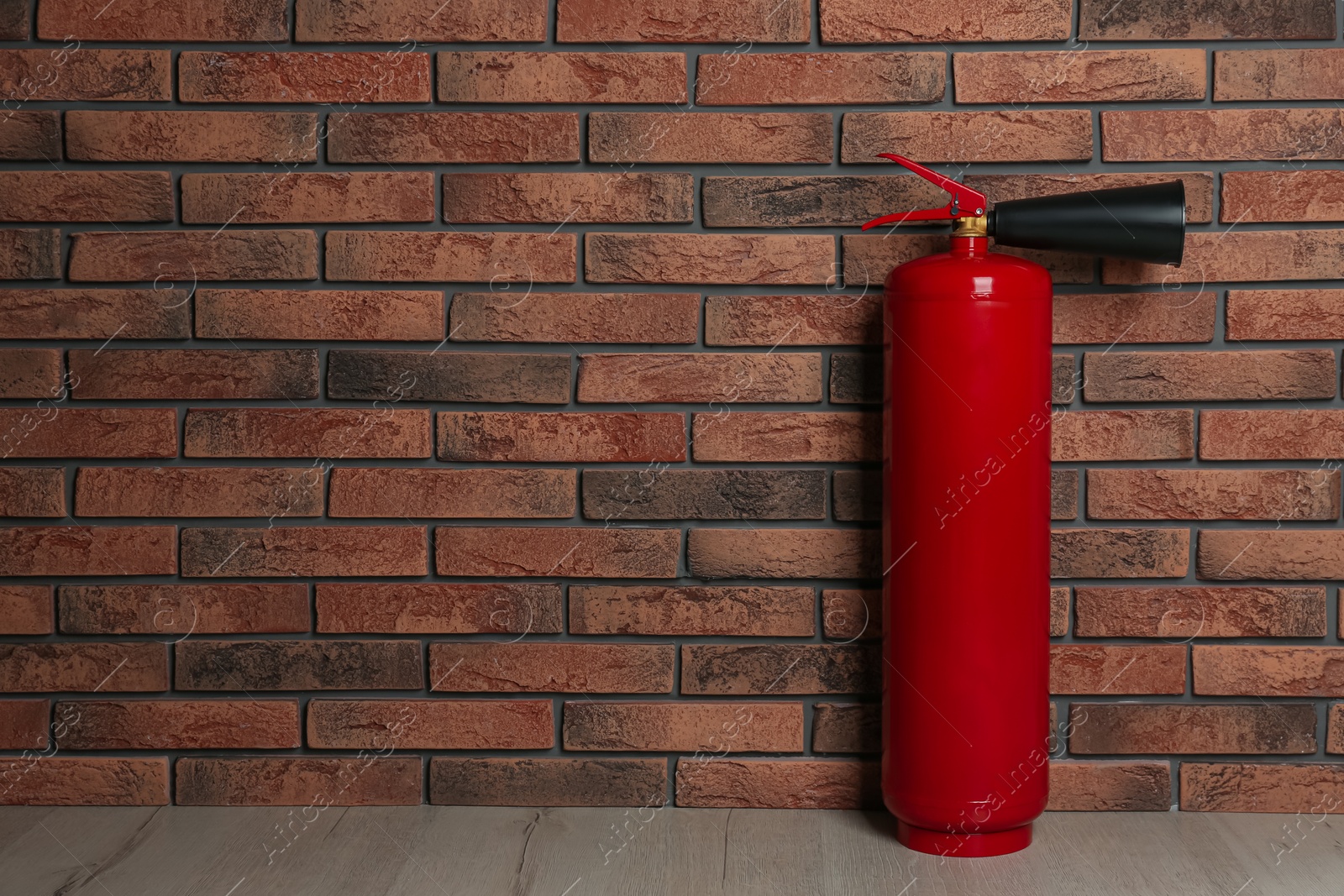 Photo of Fire extinguisher near brick wall indoors, space for text