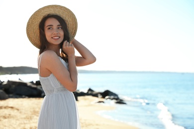 Happy young woman with hat on beach near sea. Space for text