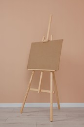 Wooden easel with blank board near beige wall indoors