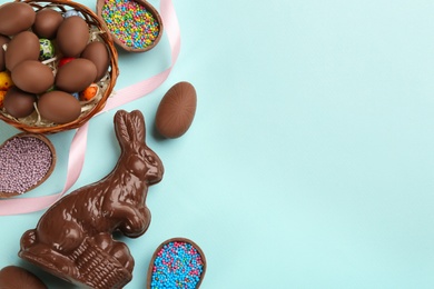 Photo of Flat lay composition with chocolate Easter bunny, eggs and candies on light blue background. Space for text
