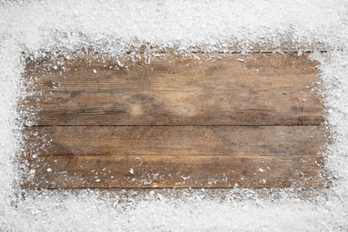 Frame made of snow on wooden background, top view with space for text. Christmas season