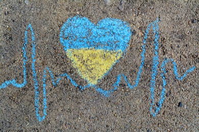 Photo of Cardiogram line with heart drawn by blue and yellow chalk on asphalt, top view