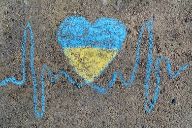 Cardiogram line with heart drawn by blue and yellow chalk on asphalt, top view