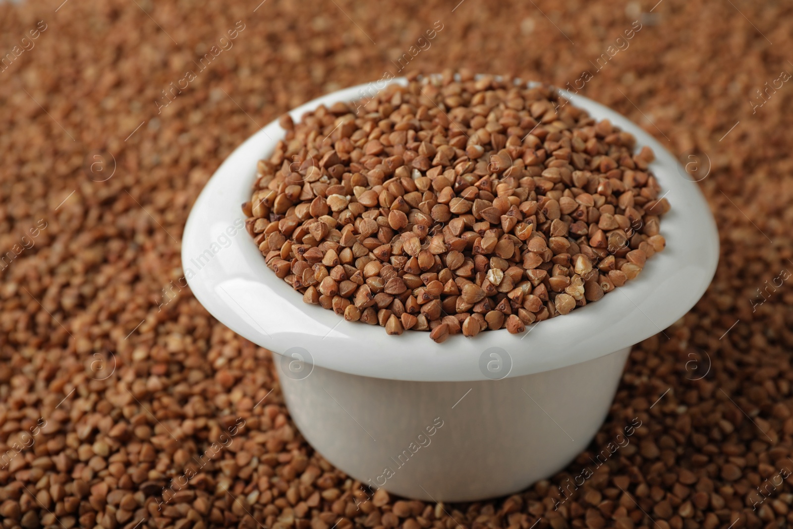 Photo of Uncooked buckwheat in bowl on grains. Organic wholesome product