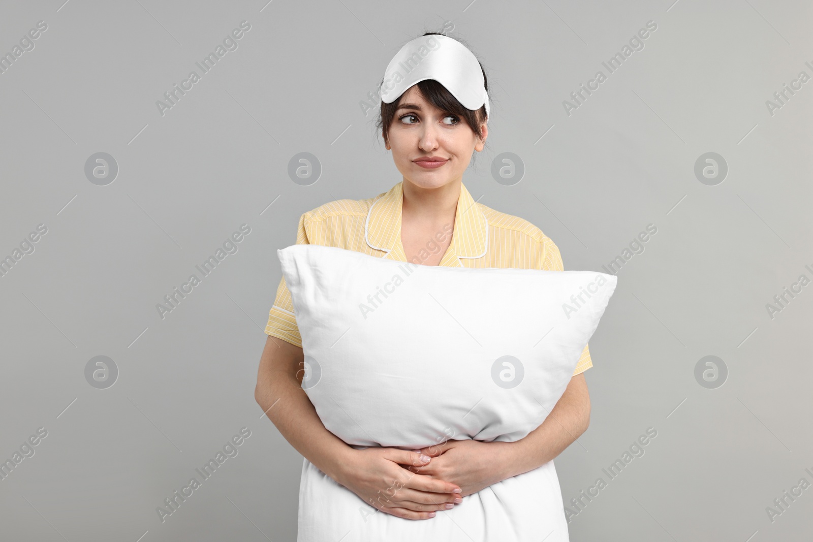 Photo of Woman in pyjama and sleep mask holding pillow on grey background