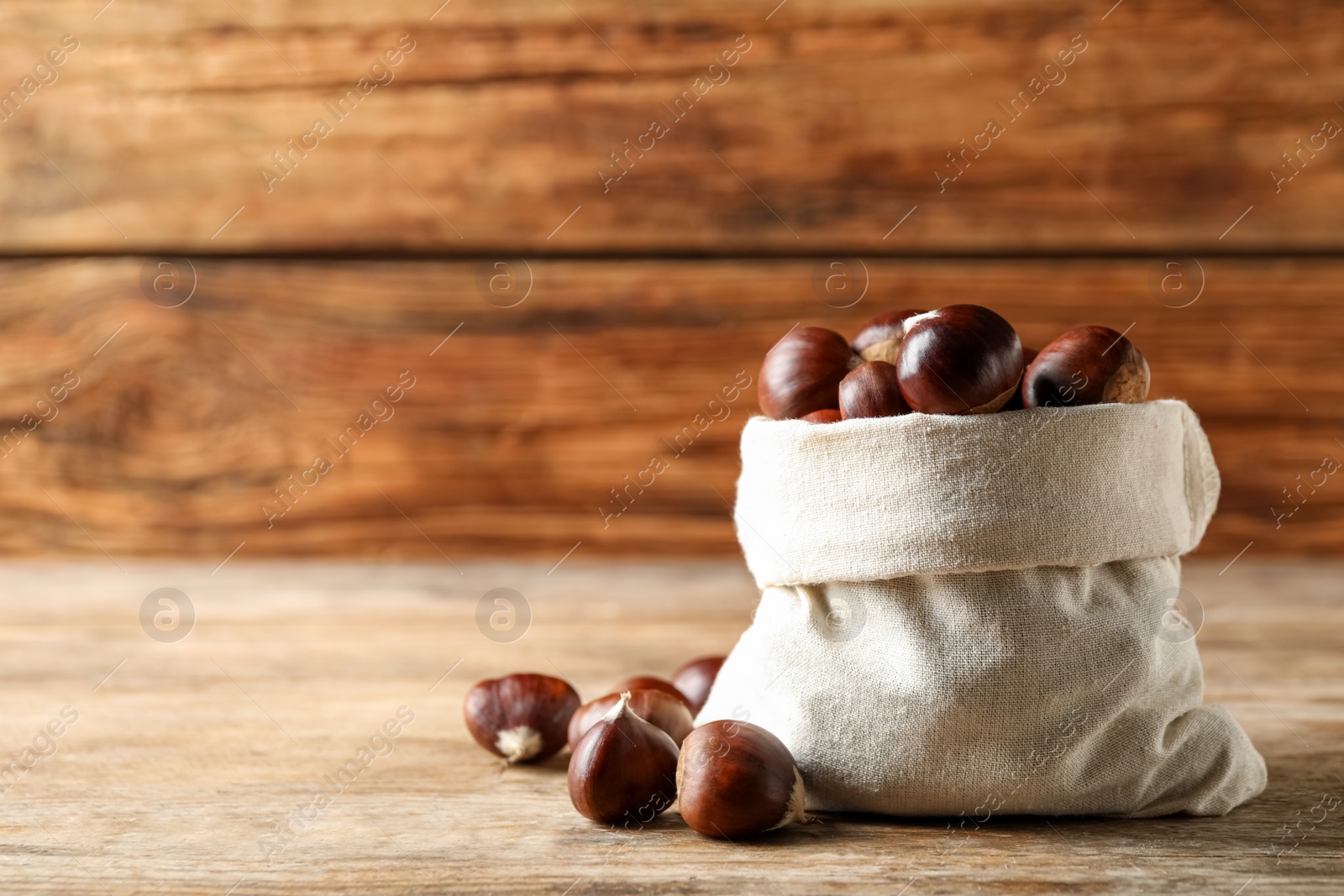 Photo of Fresh sweet edible chestnuts in sack on wooden table. Space for text