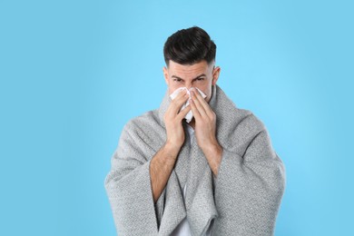Man with blanket suffering from runny nose on light blue background