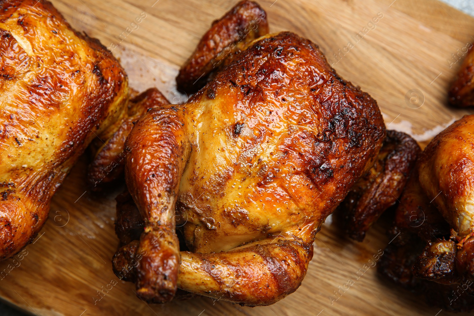 Photo of Delicious grilled whole chickens on wooden board, closeup