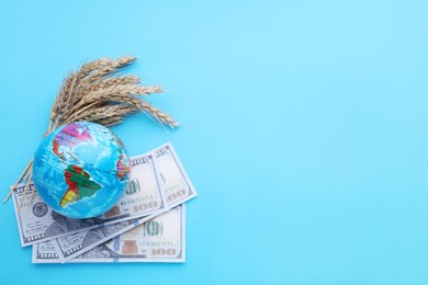 Photo of Import and export concept. Globe, ears of wheat and banknotes on light blue background, flat lay. Space for text