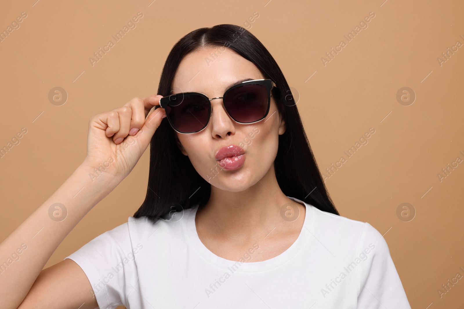 Photo of Beautiful young woman in stylish sunglasses blowing kiss on beige background