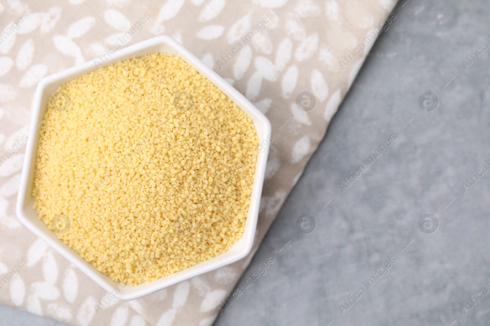 Photo of Raw couscous in bowl on gray table, top view. Space for text