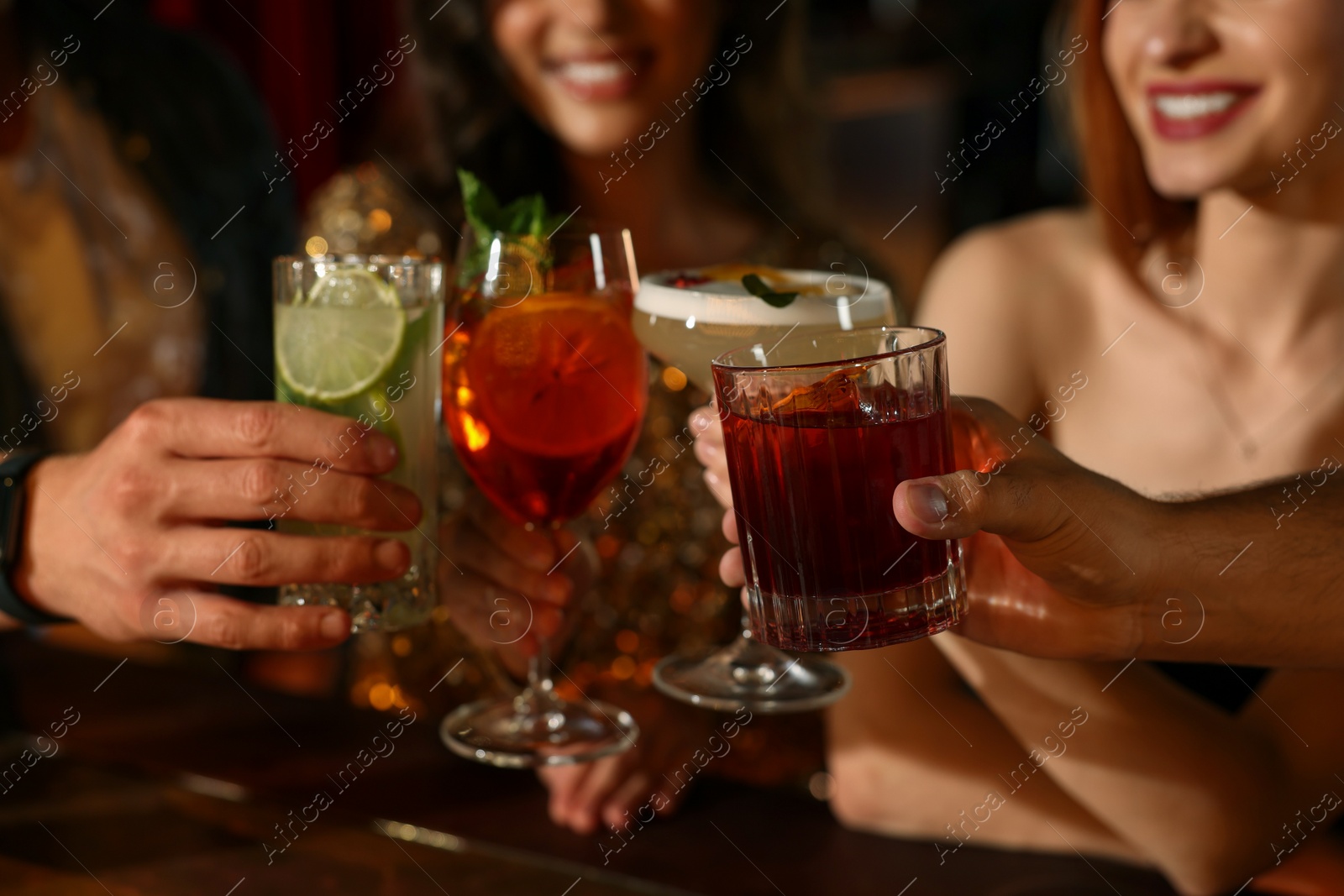 Photo of Friends clinking glasses with fresh cocktails in bar, closeup