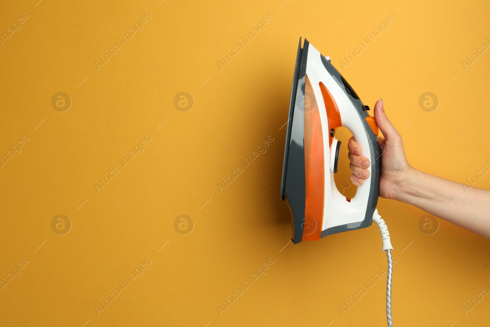 Photo of Woman holding modern iron on orange background, closeup. Space for text