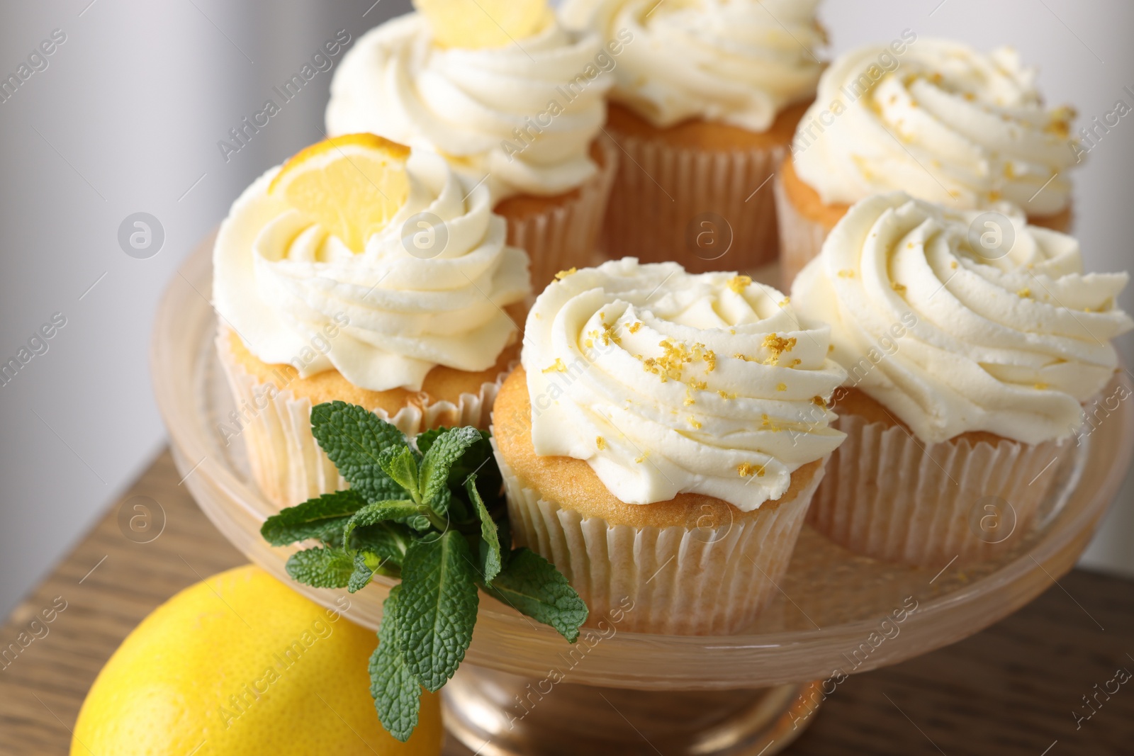 Photo of Delicious lemon cupcakes with white cream and mint on table, closeup