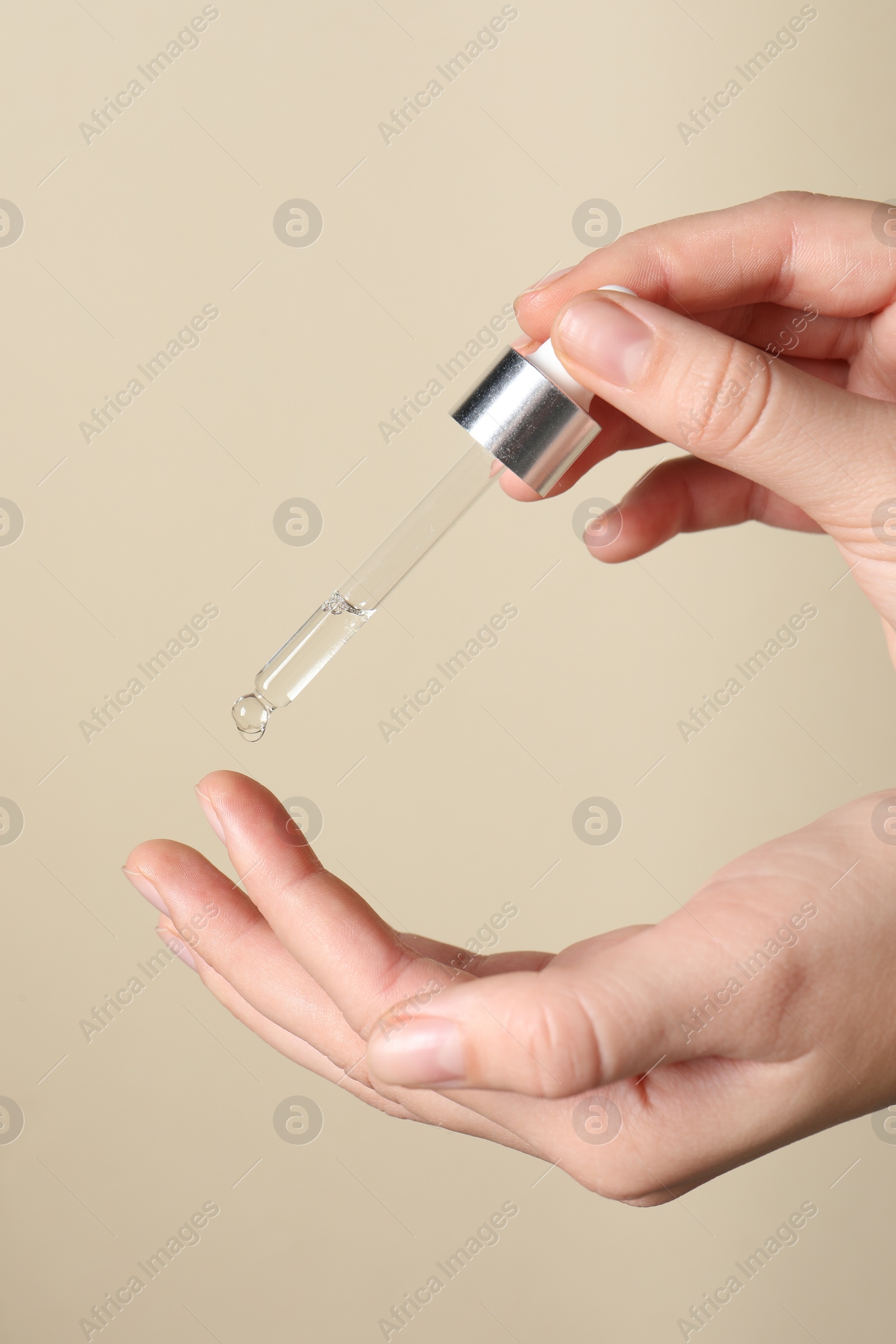 Photo of Woman applying cosmetic serum onto finger on beige background, closeup