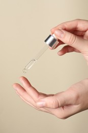 Photo of Woman applying cosmetic serum onto finger on beige background, closeup